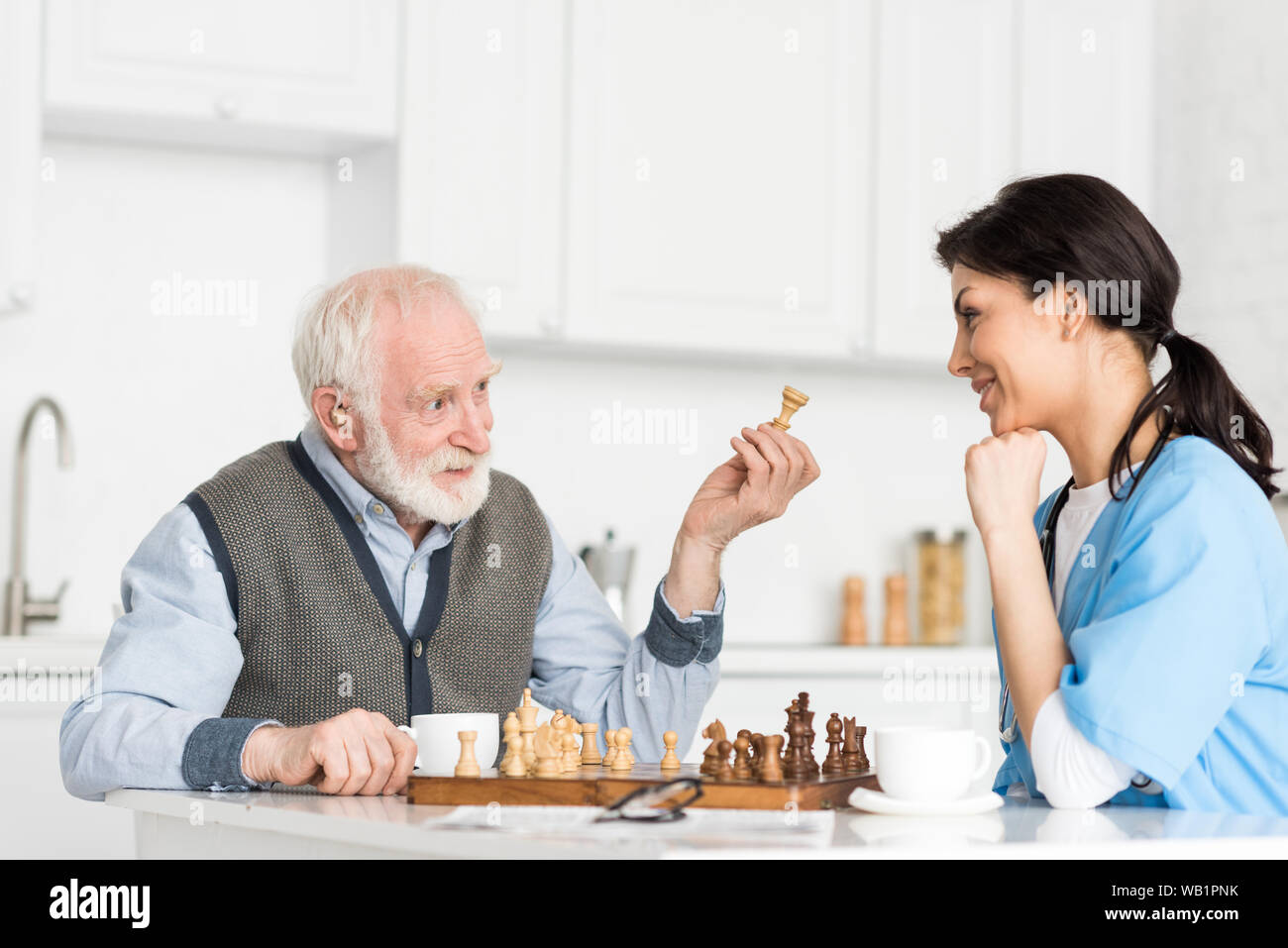 Krankenschwester und grauhaariger Mann sitzt auf helle Küche, und das Spielen in Schach Stockfoto