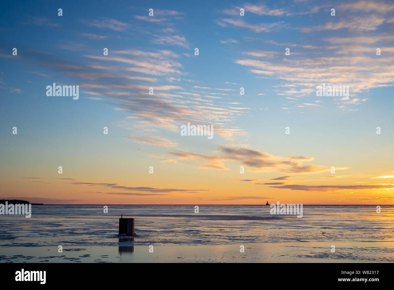 Die Sonne über einen gefrorenen Hafen und ein Eis angeln shack in ländlichen Prince Edward Island, Kanada. Leuchtturm am Horizont. Stockfoto