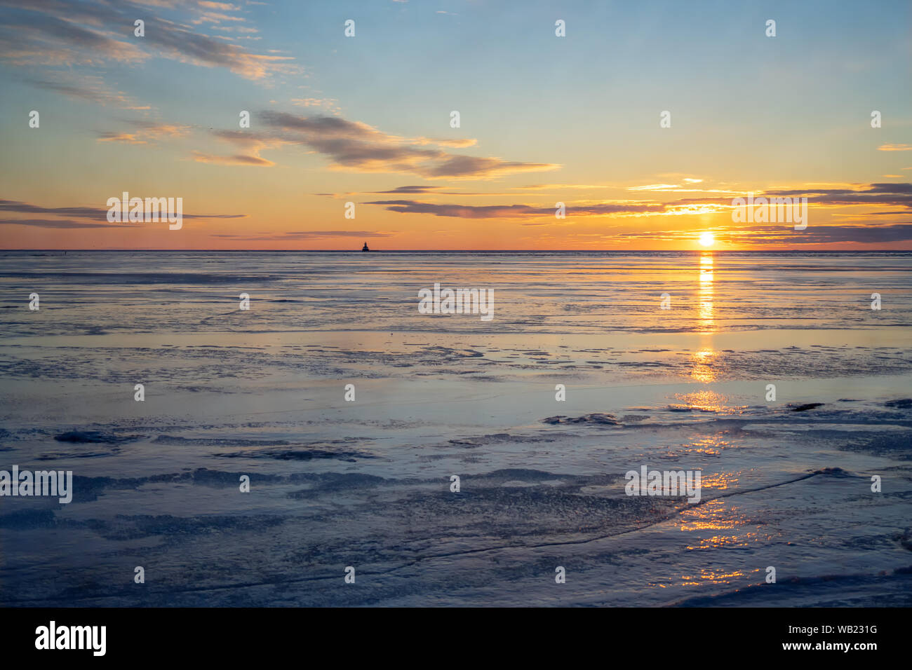 Die Sonne über einen gefrorenen Hafen in ländlichen Prince Edward Island, Kanada. Leuchtturm am Horizont. Stockfoto