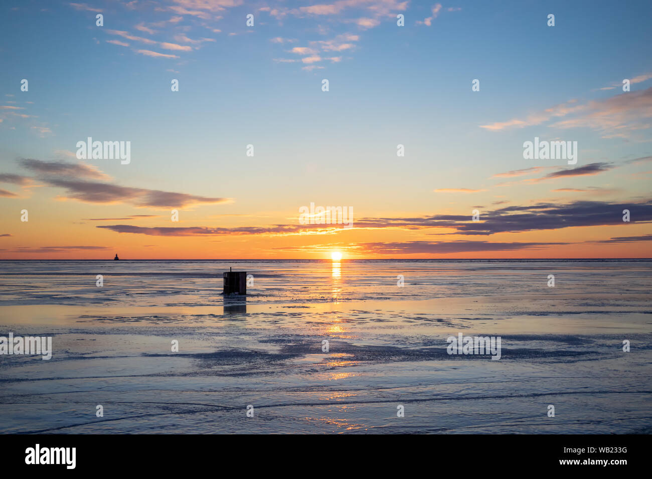 Die Sonne über einen gefrorenen Hafen und ein Eis angeln shack in ländlichen Prince Edward Island, Kanada. Leuchtturm am Horizont. Stockfoto
