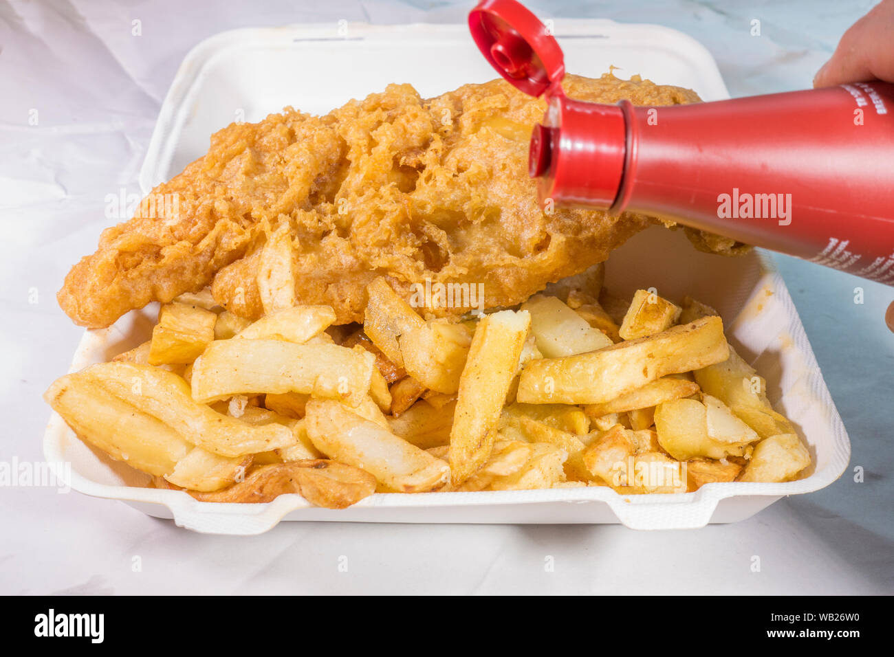 Schließen Sie Aufnahme einer Mahlzeit zum Mitnehmen von Frittierten zerschlagene Fish und Chips mit Essig. Stockfoto