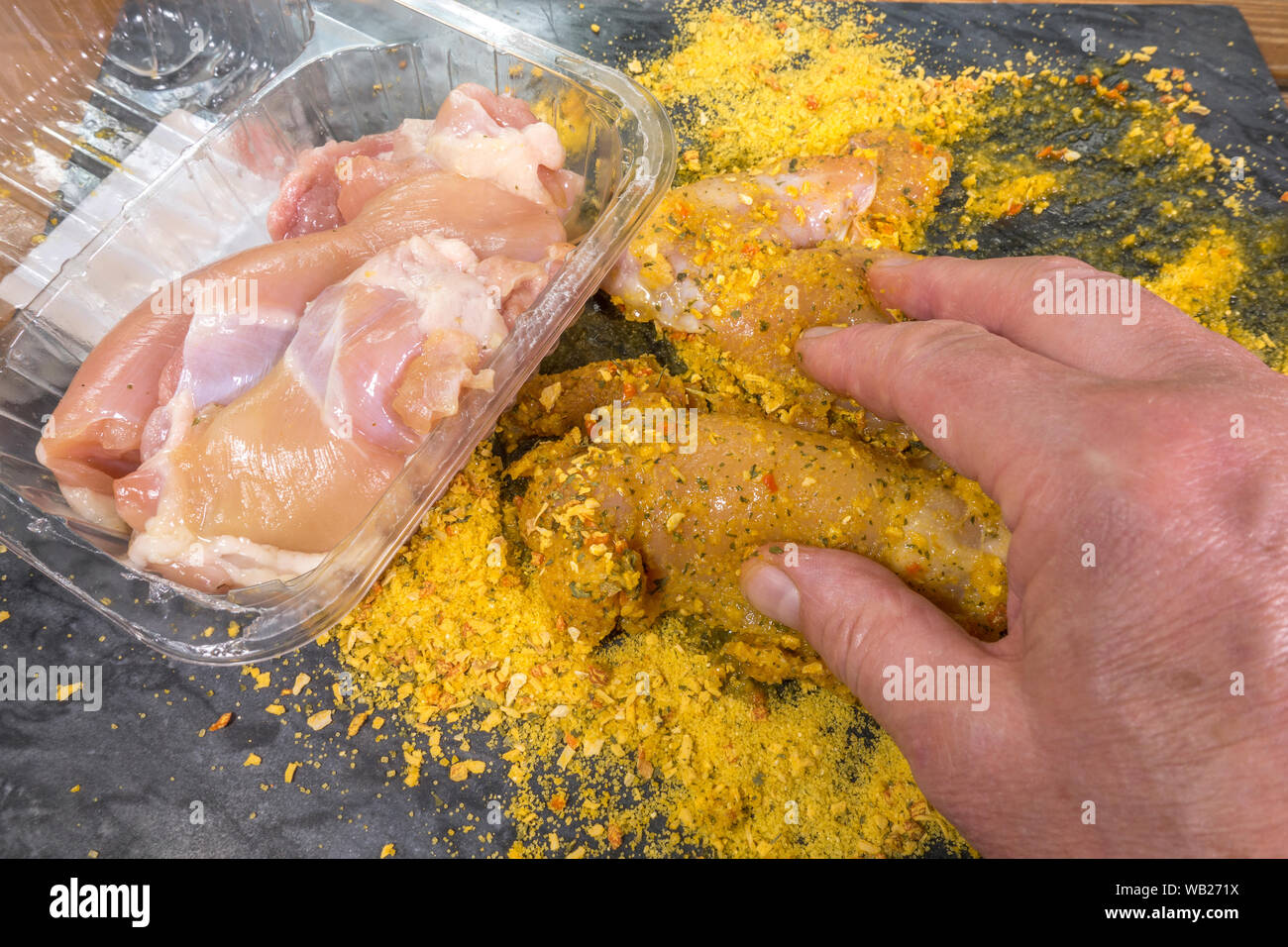 Schließen overhead Shot der Hände Beschichtung Stück eines Mannes von rohem Huhn mit einem trockenen Würzmischung, bereit, für das Kochen. Stockfoto