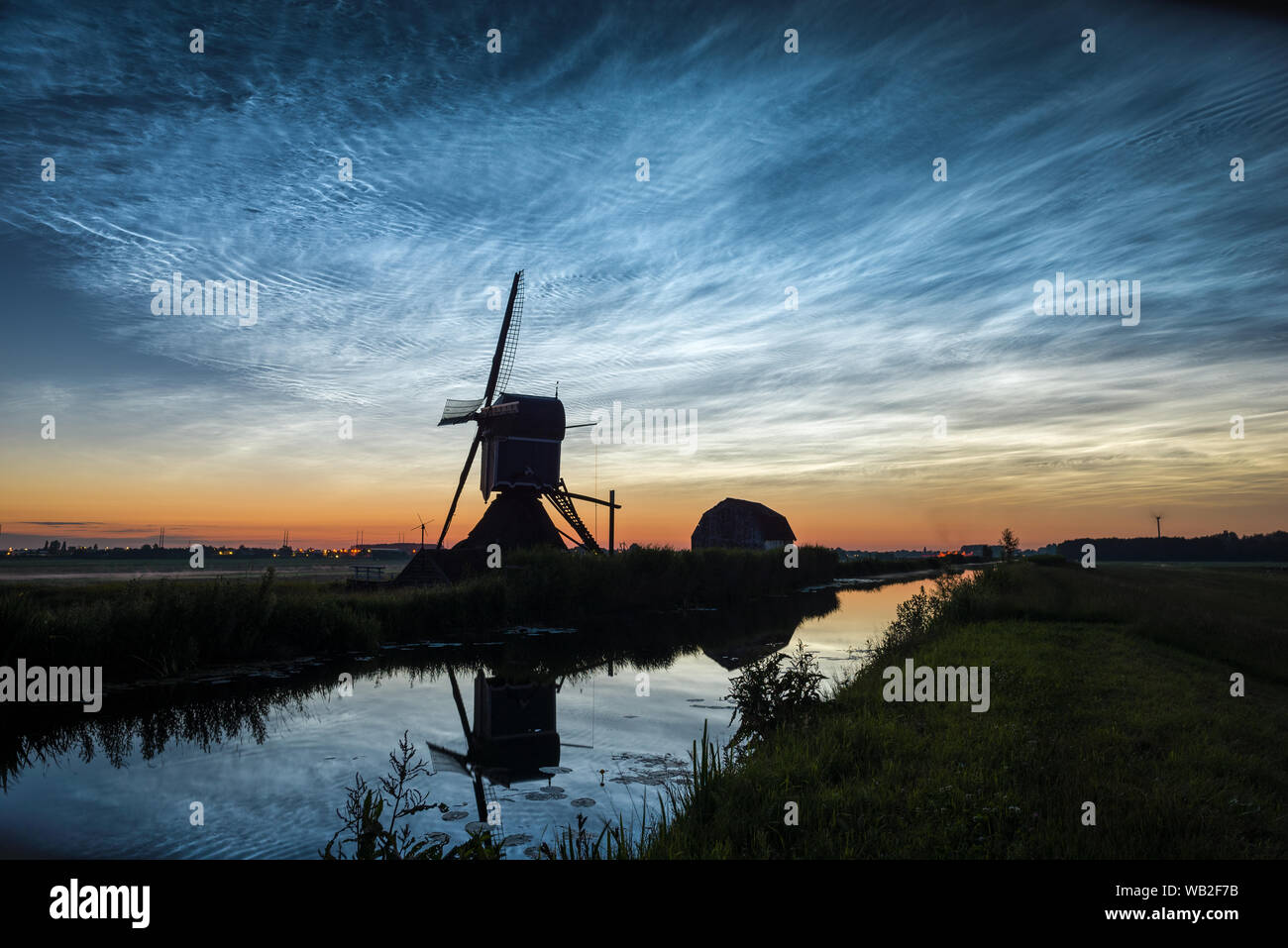 Nachtaktive Wolken (NLC), Blick nach Norden in der Mittsommernacht. Klassische holländische Szene mit Kanal- und Windmühlensilhouette gegen den Dämmerungshimmel. Stockfoto