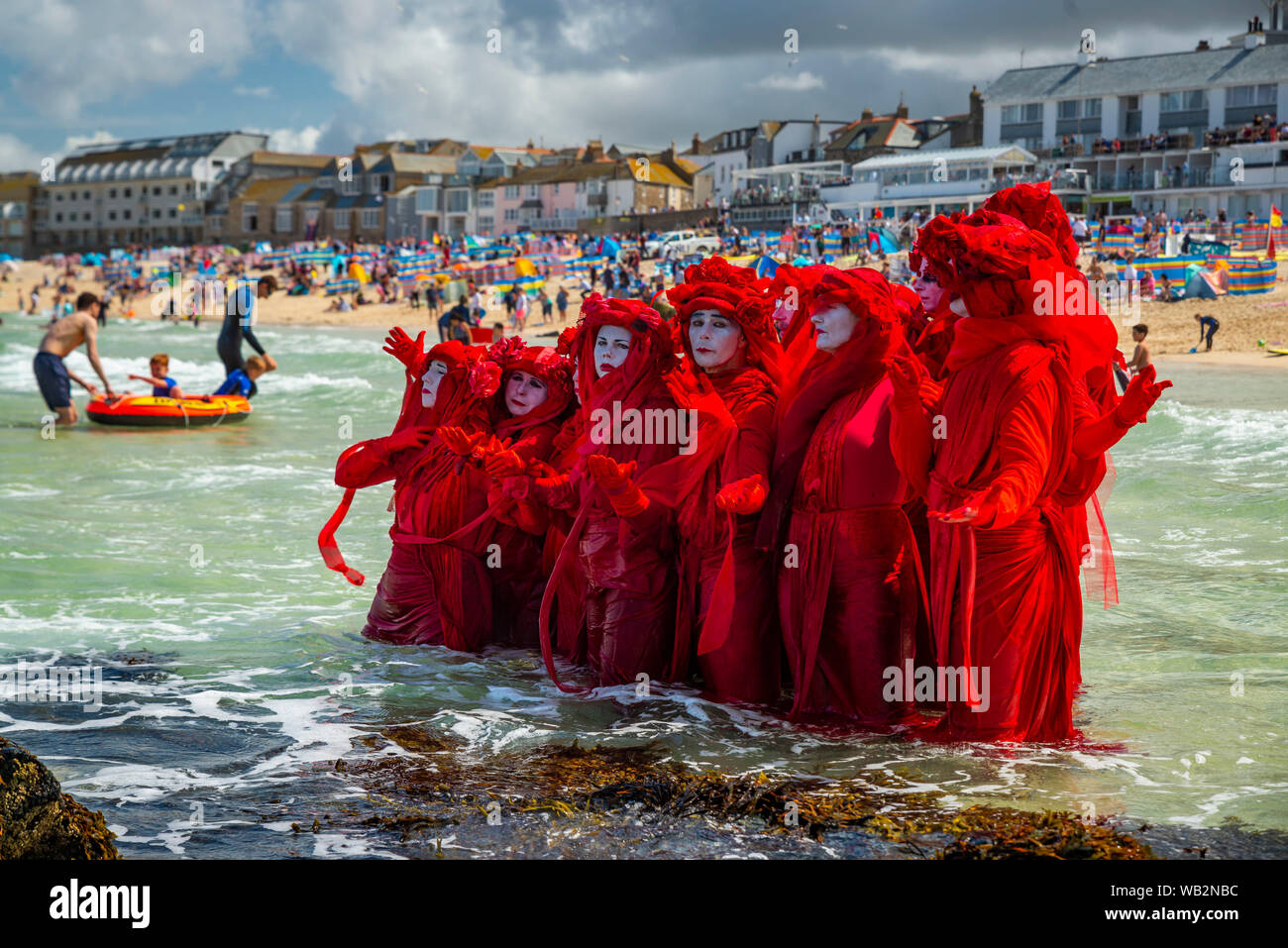 Porthmeor, St Ives, Cornwall, UK. Leistung protest Truppe der Roten Rebellen Brigade Spaziergang zwischen Urlauber tasing Bewusstsein für die Klimakrise. Stockfoto