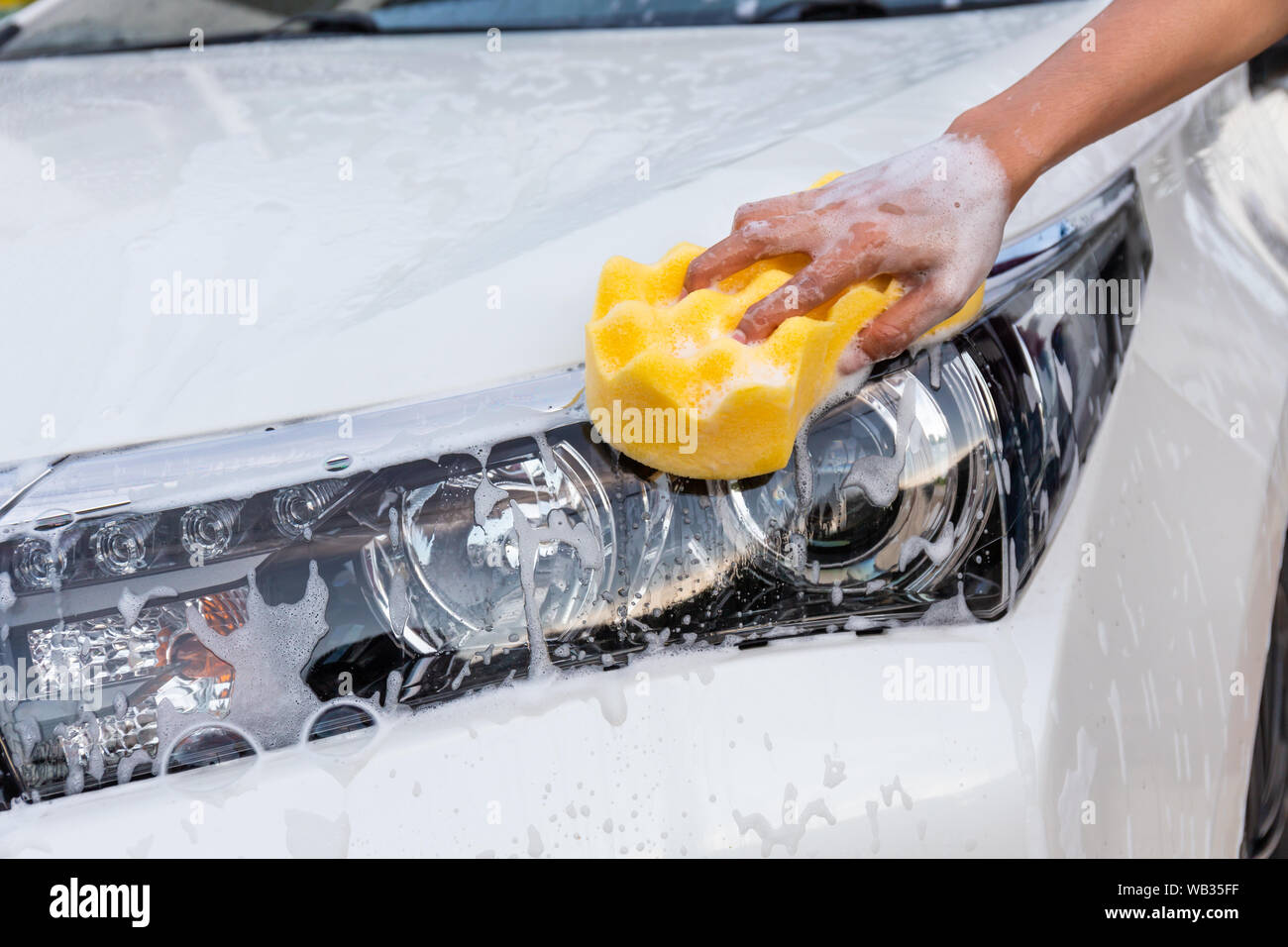 Frau hand mit gelben Schwamm waschen Scheinwerfer modernes Auto oder Reinigung Automobil. Auto waschen Konzept Stockfoto