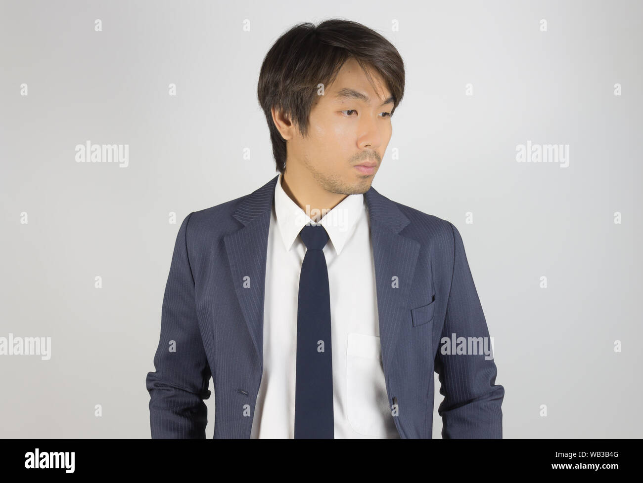 Jungen asiatischen Porträt Unternehmer im blauen Anzug auf der Suche unten auf grauem Hintergrund Stockfoto