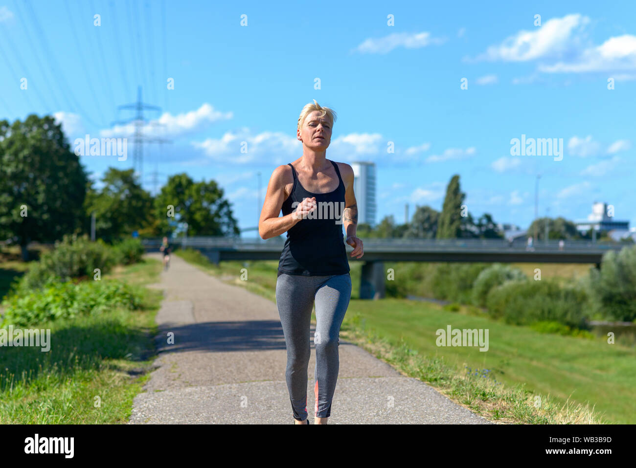 Frau Joggen im Freien im Sommer Sonne nähert sich die Kamera in einem niedrigen Winkel drei Viertel Ansicht konzeptionelle Gesundheit und Fitness Stockfoto