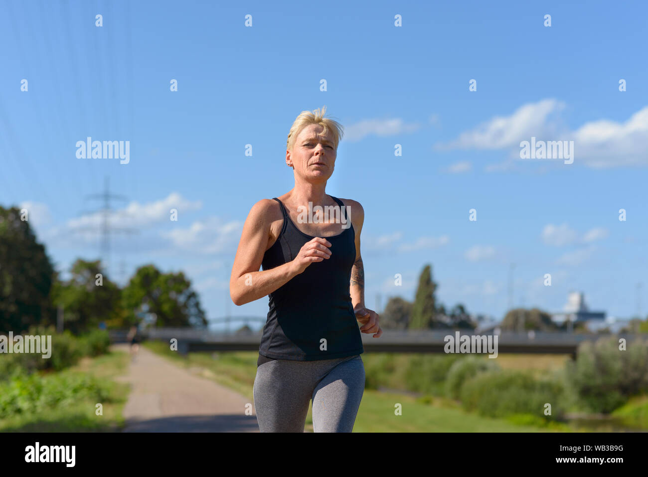 Frau Joggen im Freien im Sommer Sonne nähert sich die Kamera in einem niedrigen Winkel drei Viertel Ansicht konzeptionelle Gesundheit und Fitness Stockfoto