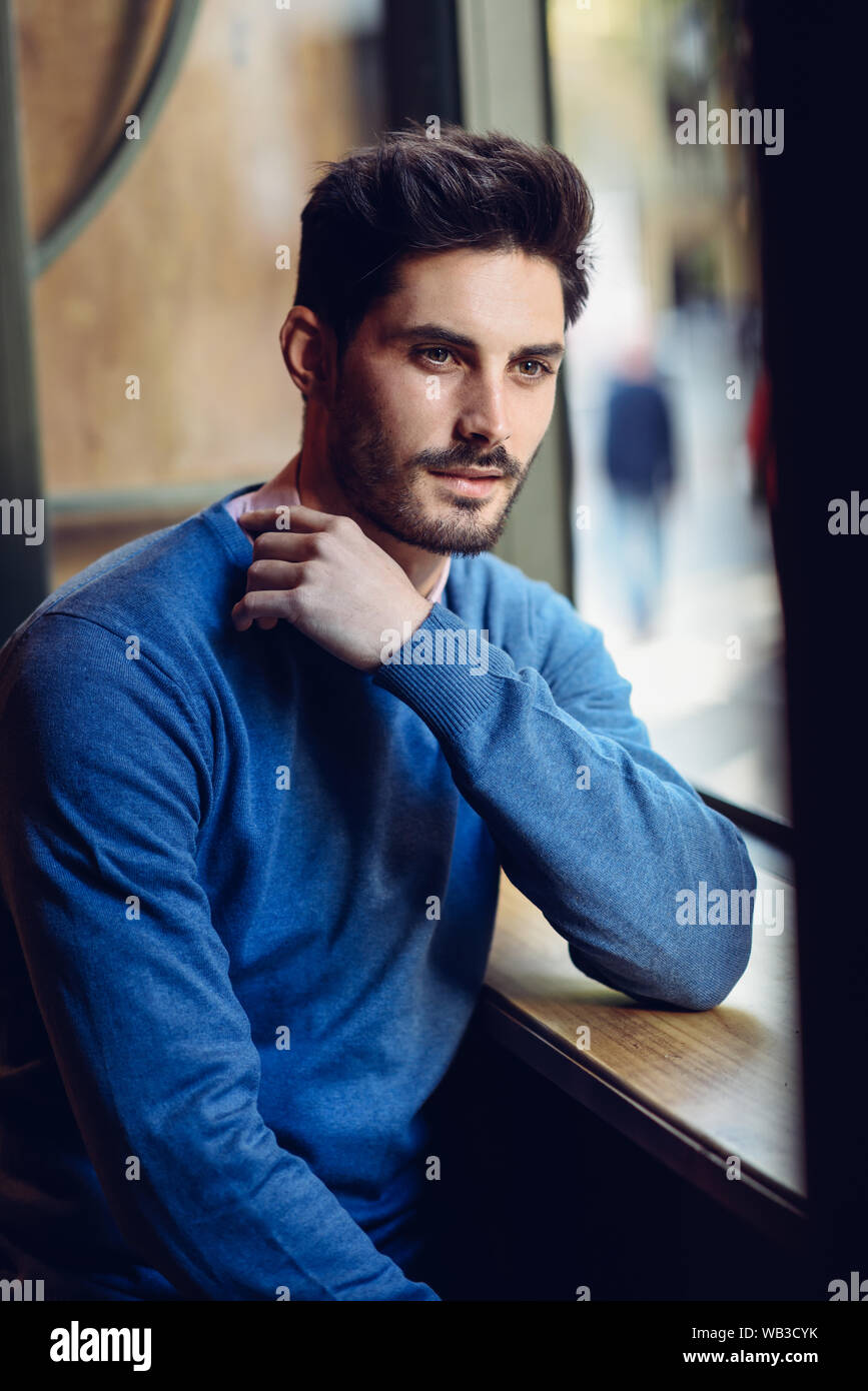 Nachdenklicher Mann mit blauen Pullover mit verloren, Suchen in der Nähe eines Fensters Stockfoto