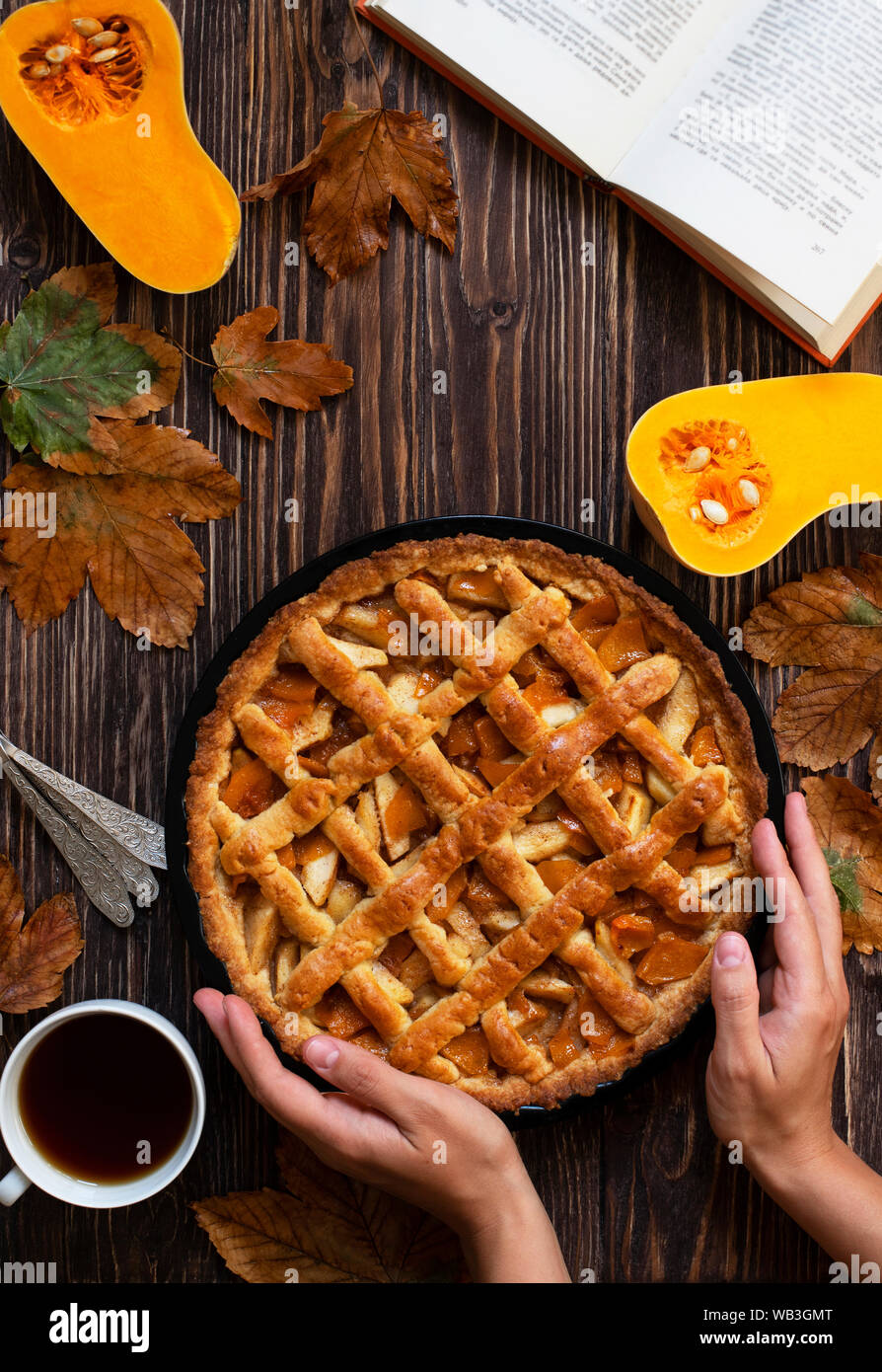 Weibliche Hände halten hausgemachte Kürbiskuchen. Halloween und Thanksgiving. Urlaub Kürbis Süßigkeiten. Holz Herbst Hintergrund, trockene Blätter, schneiden Kürbis, Kaffee Stockfoto