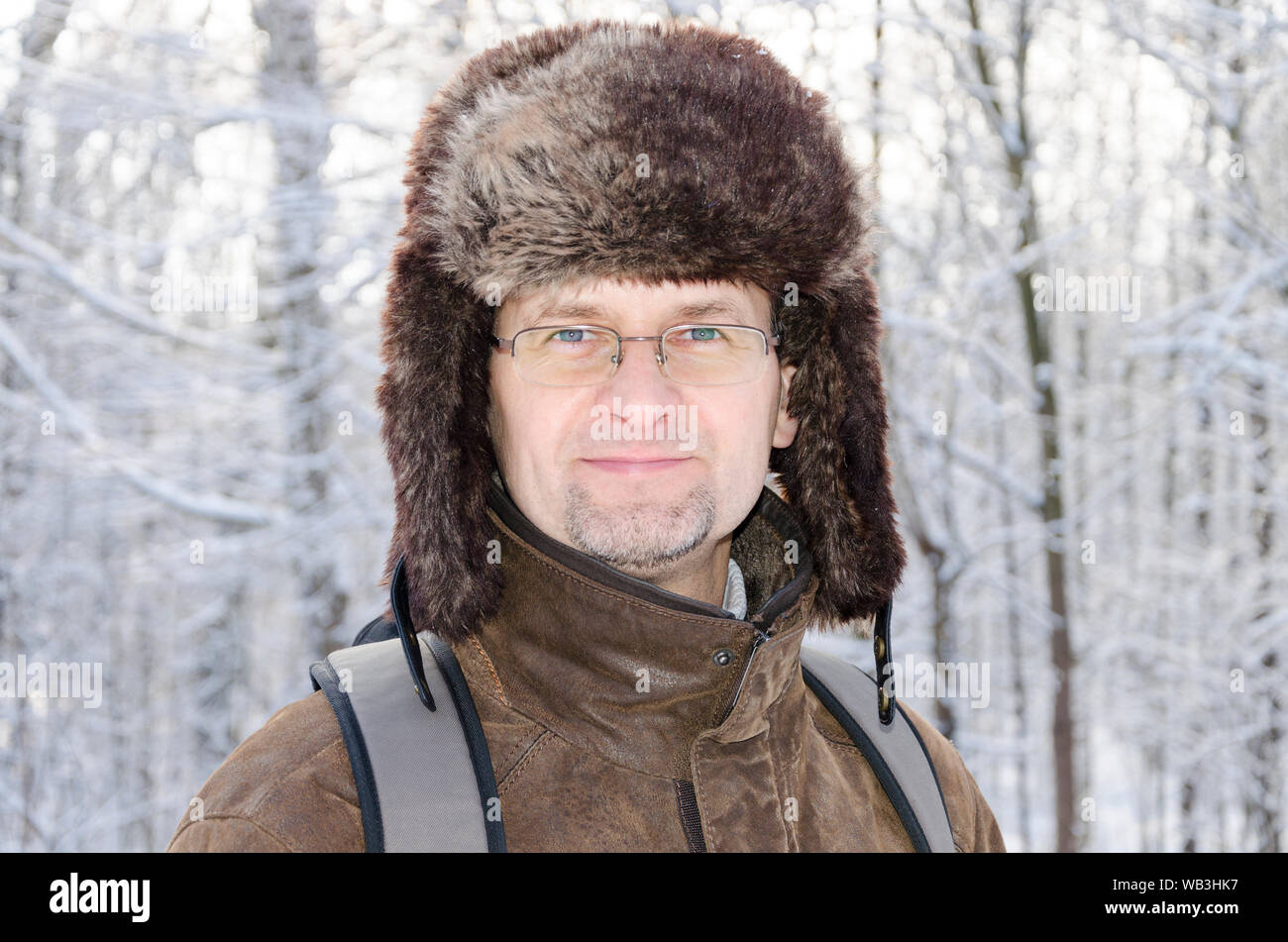 Aportrait eines Mannes in Gläsern in einer pelzkappe trägt einen Rucksack in der verschneiten Winterlandschaft Stockfoto