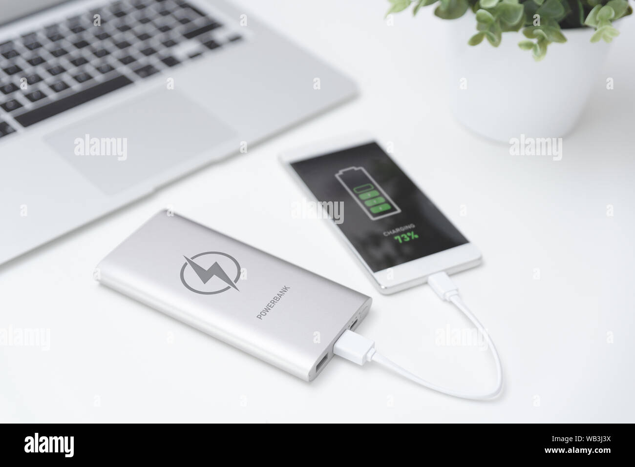 USB-Ladegerät angeschlossen zu Smart Phone. Power Bank, Handy Akku auf Schreibtisch Konzept Stockfoto