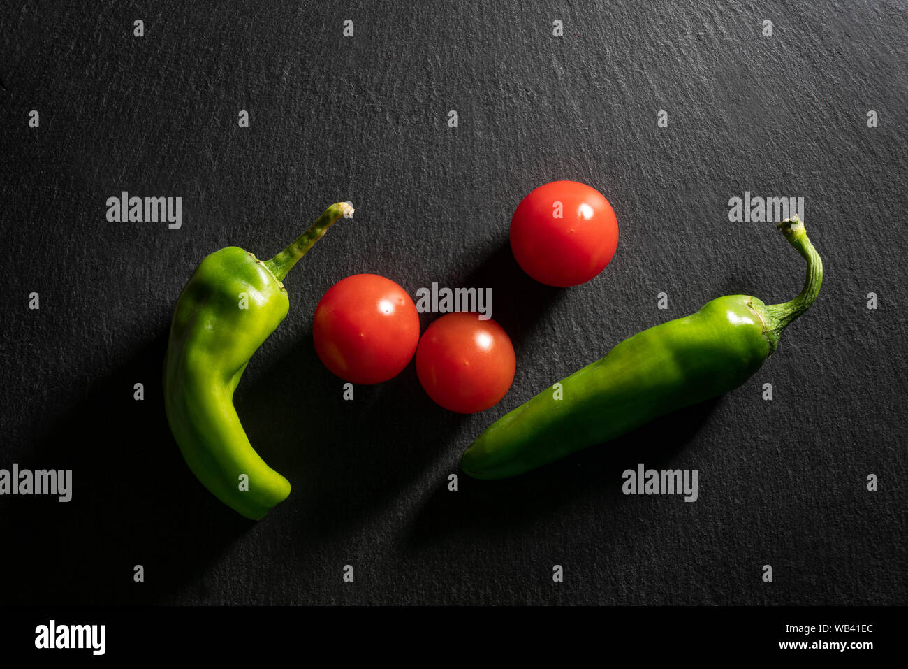 Einige Tomaten und zwei grüne Paprika auf einem schwarzen Stein saurface Stockfoto