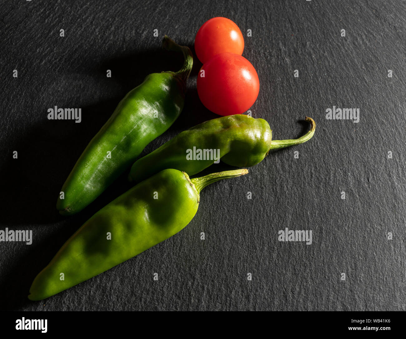 Einige Tomaten und zwei grüne Paprika auf einem schwarzen Stein saurface Stockfoto