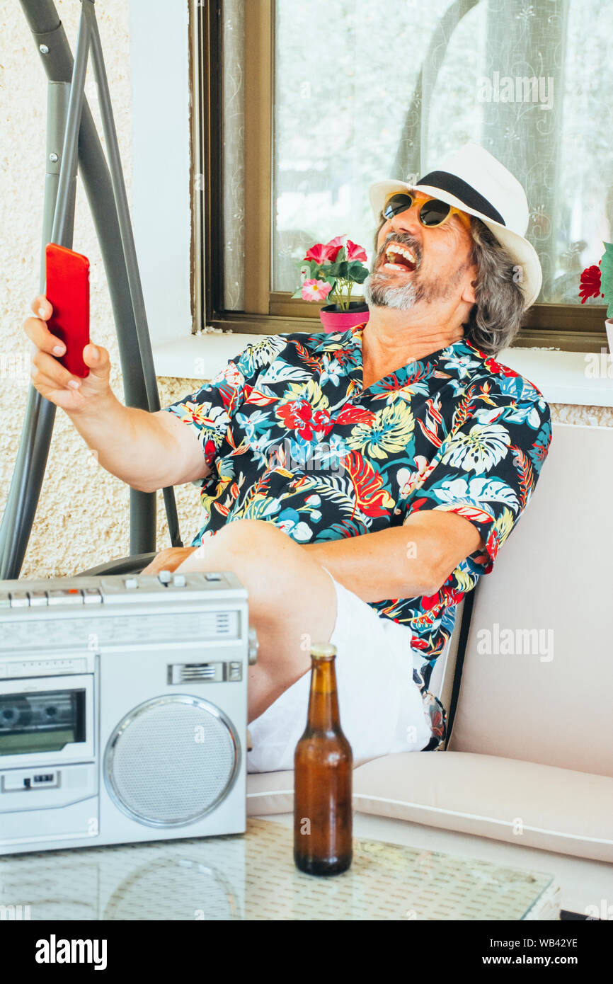 Reifer Mann Spaß mit seinem Handy, während auf einer Schaukel sitzend Stuhl mit einem Bier und Musik aus einem Radio-/Kassetten-Player Stockfoto