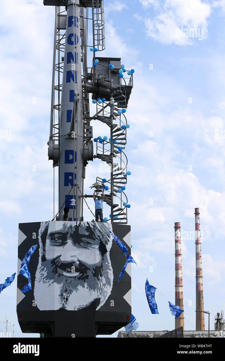 Dublin unterstützer Dekan Gaffney, ein kranführer mit Dublin Stauer, hält die Sam Maguire Cup als er steht auf dem Ronnie Drew Kran im Hafen von Dublin in Dublin für fünf Teams 'Drive', im Vorfeld der nächsten Wochenenden alle Irland Fußball Finale gegen Kerry. Stockfoto