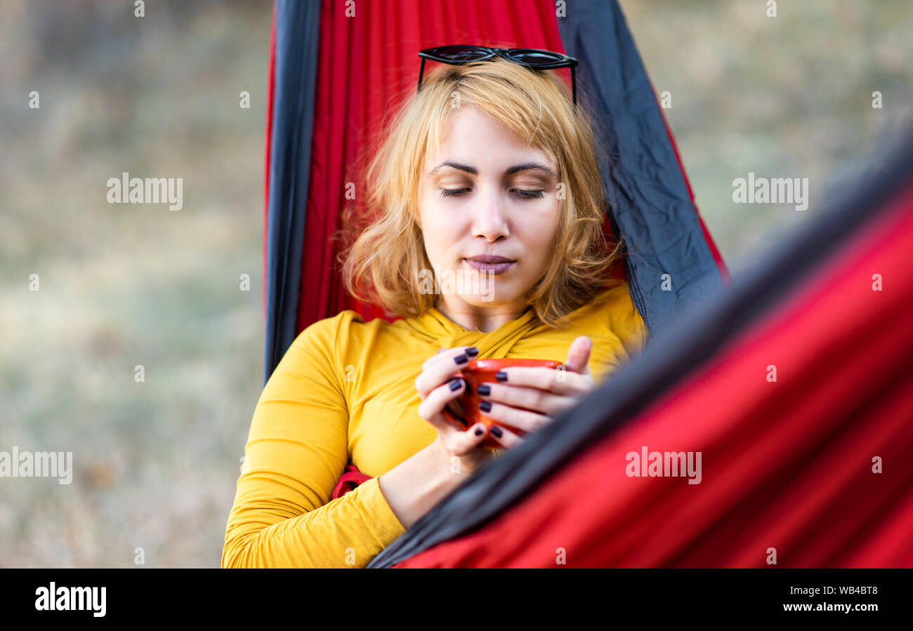 Frau in einer Hängematte Sitzen mit einer Tasse Kaffee im Freien Stockfoto