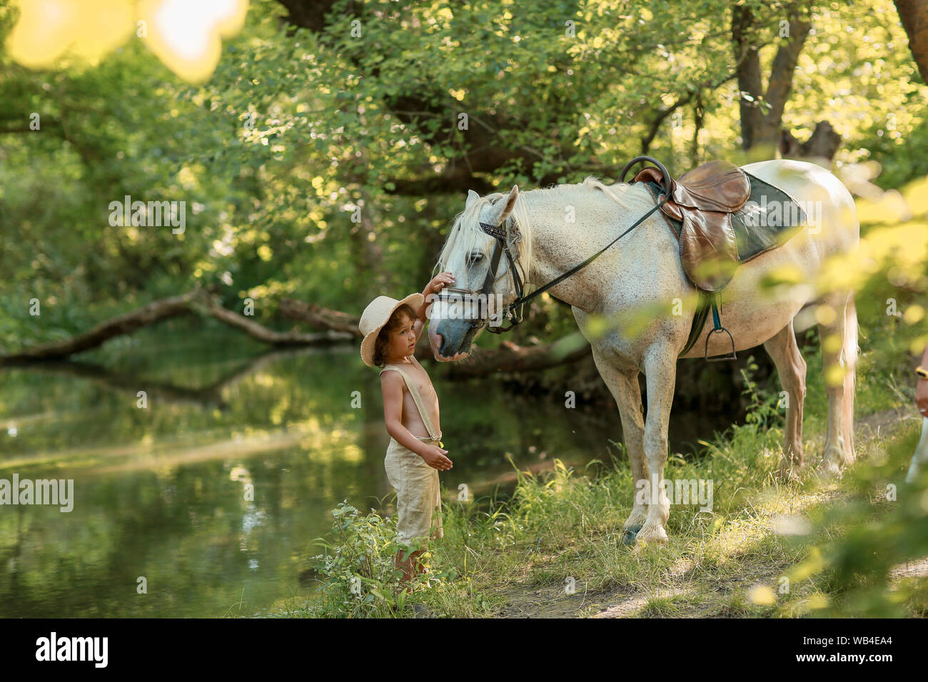 Little Baby Boy mit lockigem Haar gekleidet als Hobbit spielen mit Pferd im Sommer Wald. Stockfoto