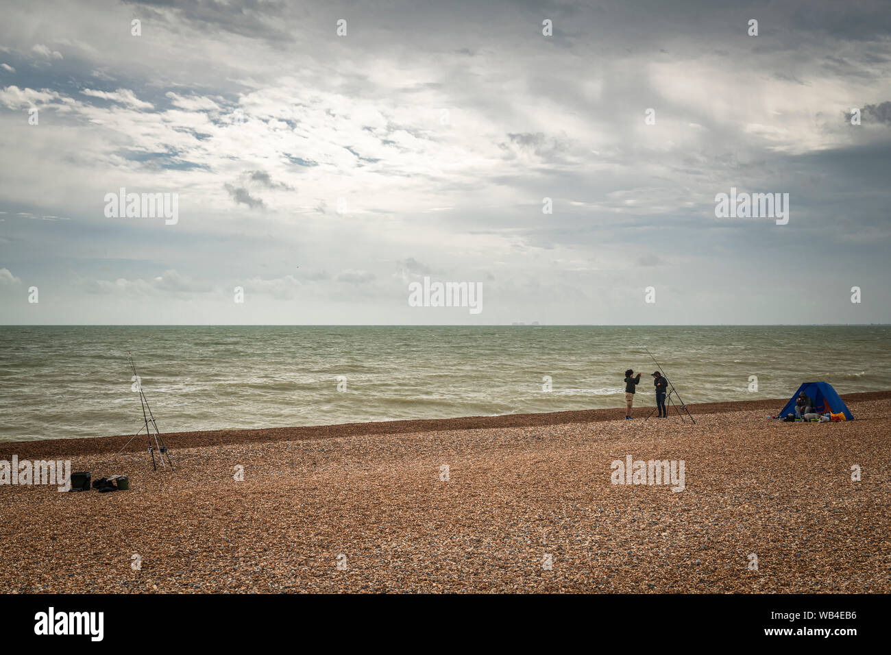 Drei Leute Angeln vom Strand in Hythe, Kent, England, an einem bewölkten Sommer am Nachmittag, den 17. August 2019 Stockfoto