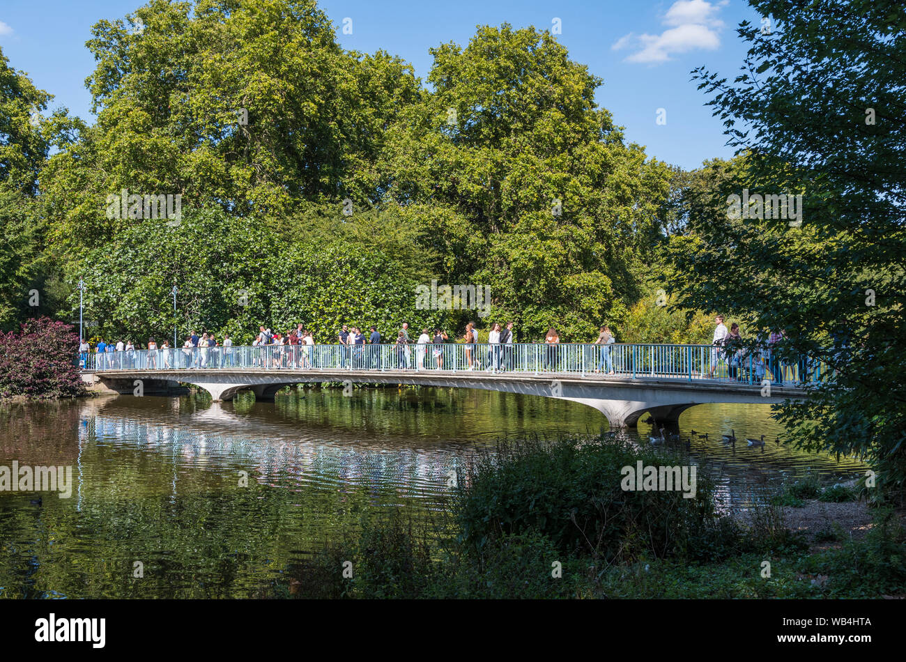 Menschen, die über die blaue Brücke, eine niedrig-gewölbte konkrete Fußgängerbrücke in St. James's Park, Westminster, London, England, UK. Stockfoto