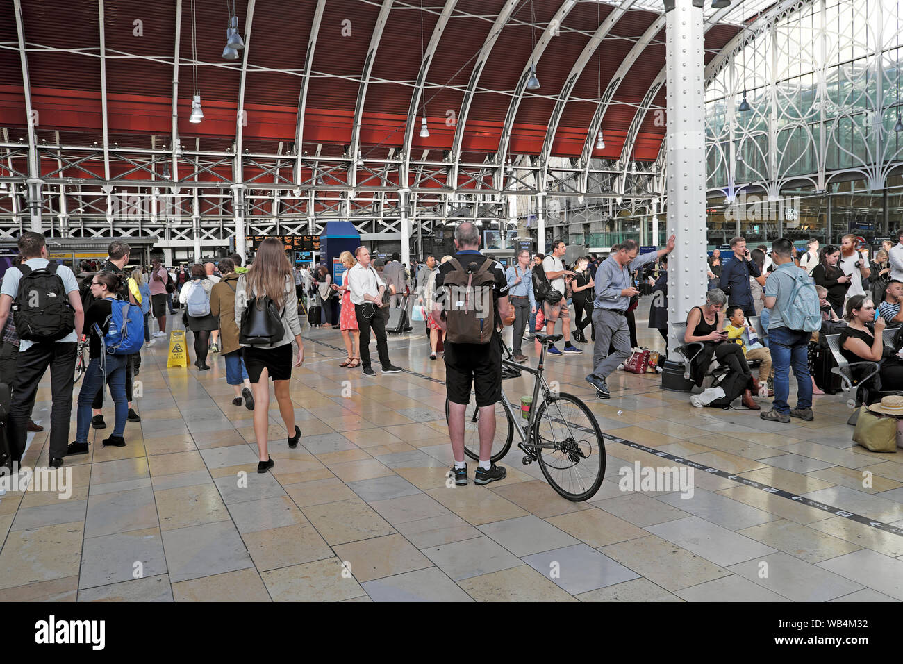Passagiere Rückansicht Radfahrer Mann mit Fahrrad Rucksack innen warten auf der belebten Bahnhofshalle am Bahnhof Paddington in London England UK KATHY DEWITT Stockfoto