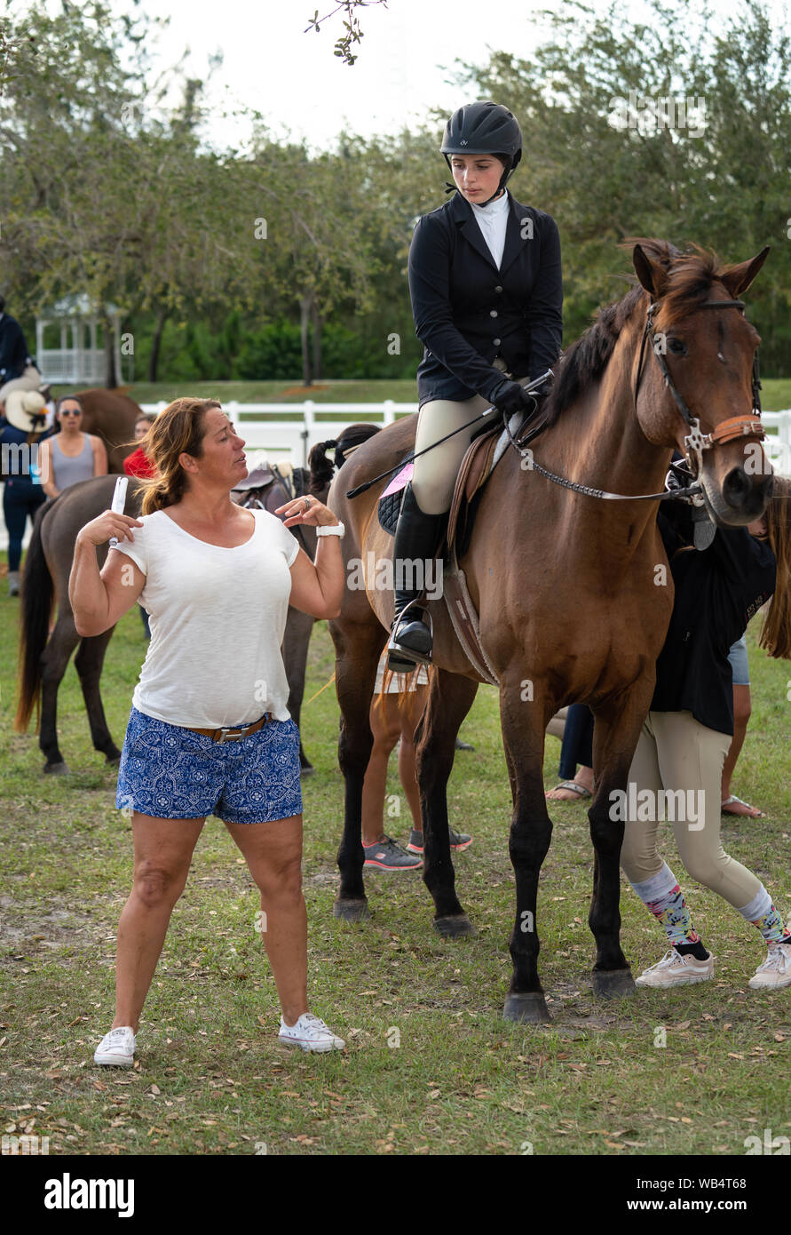 Eine weibliche Reitlehrer ist zu demonstrieren, ihre Schüler die richtige Position auf einem Pferd während ein Pferderennen Stockfoto