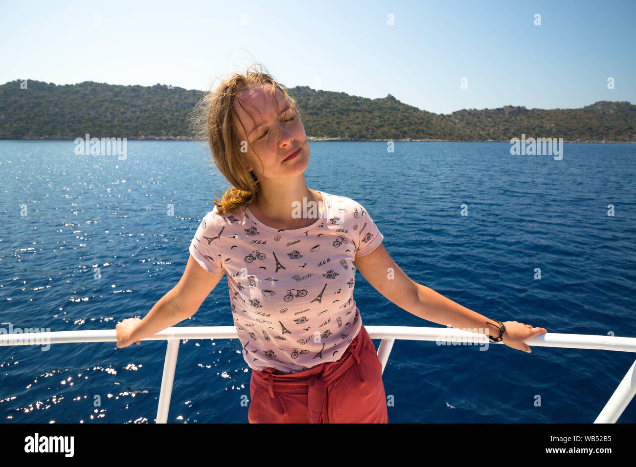 Schöne und junge Mädchen auf einer Yacht. Ein Mädchen steht mit ihren Augen von der hellen Sonne geschlossen. Hinter dem Rücken der Mädchen ist ein klares Meer. Stockfoto