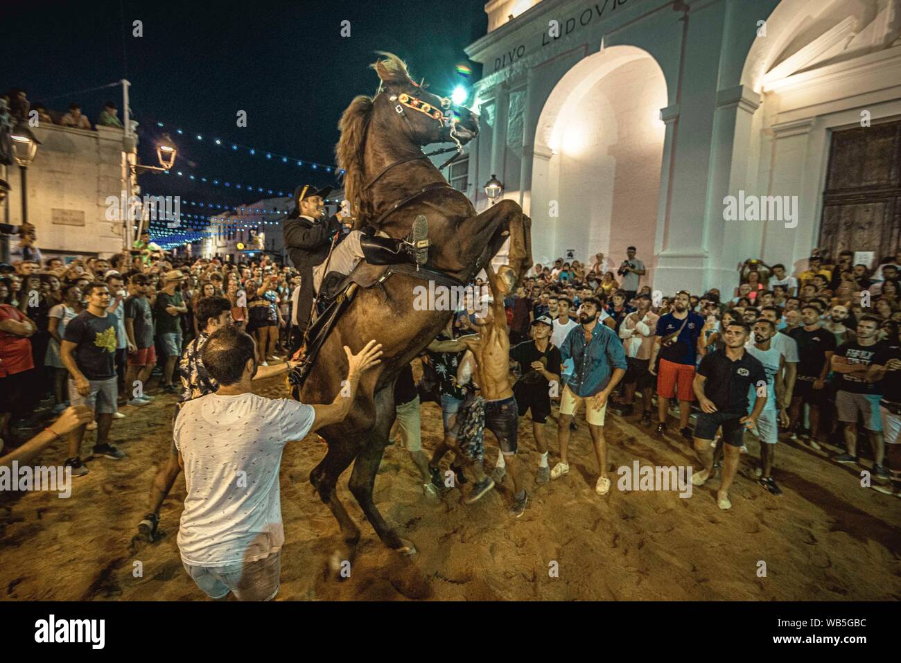 Sant Lluis, Spanien. 24 August, 2019: Ein "caixer' (Reiterin) bäumt sich auf seinem Pferd von einer jubelnden Menge während des traditionellen "JALEO" umgeben in Sant Lluis Festival. Stockfoto