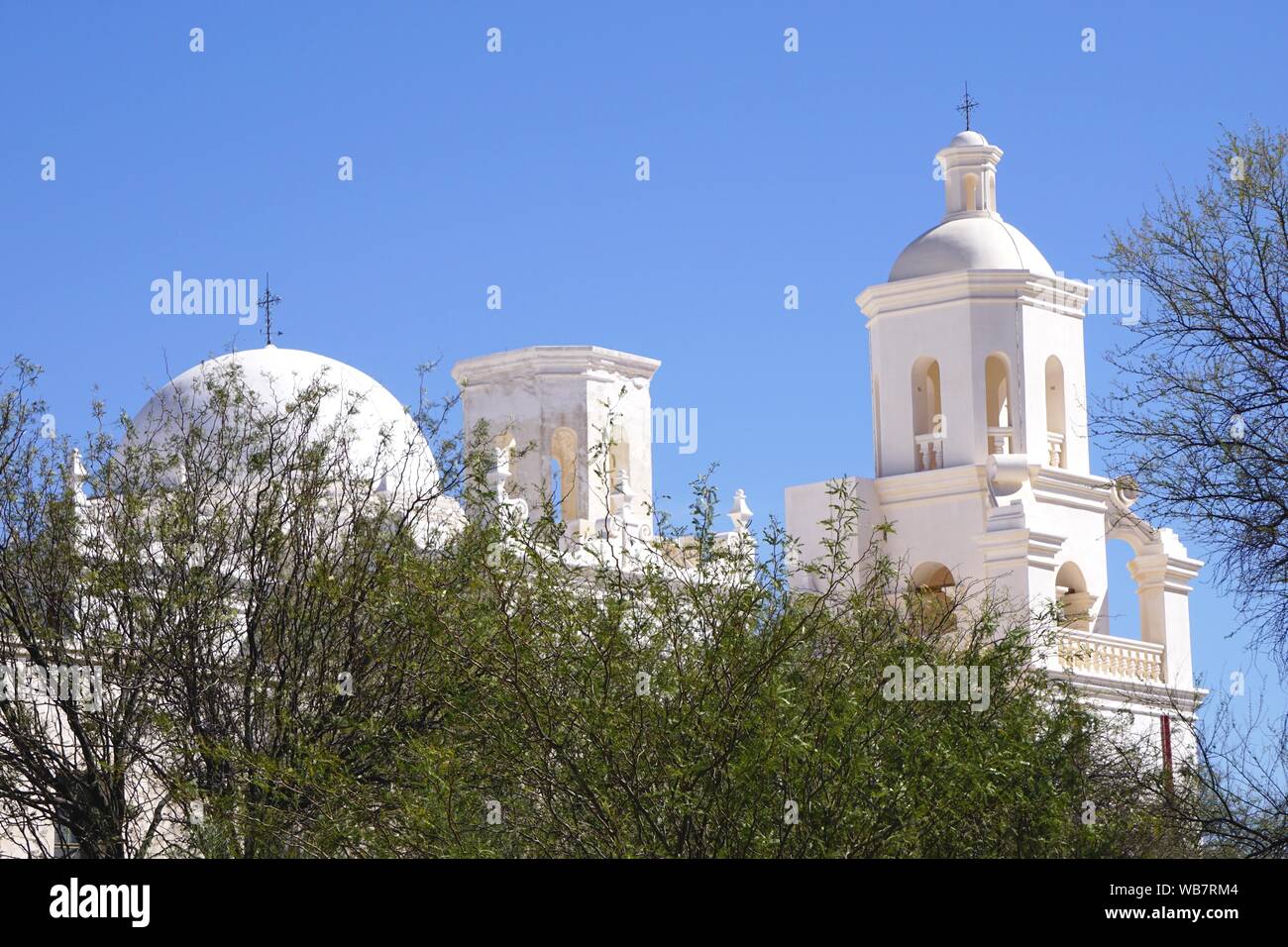 Die historische Mission San Xavier, die sich außerhalb von Tucson, Arizona, befindet, ist über das Frühlingslaub hinaus in Silhouette gegen einen klaren blauen Himmel zu sehen. Stockfoto