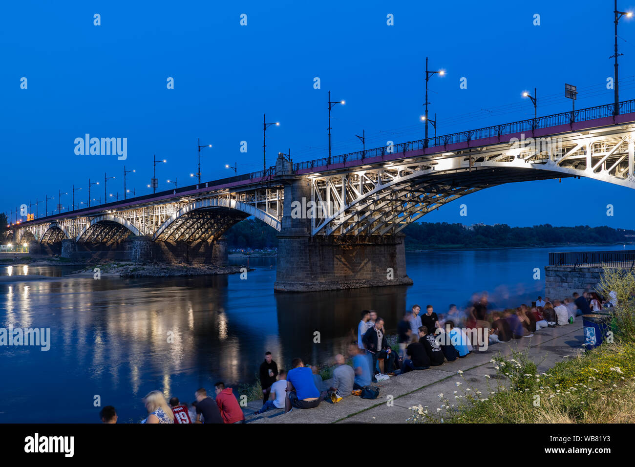 Warschau, Polen - 20. Juli 2019: Gruppe von Menschen an der Weichsel waterfront Entspannen durch die poniatowski Brücke (Polnisch: Die meisten Poniatowskiego) Illumina Stockfoto