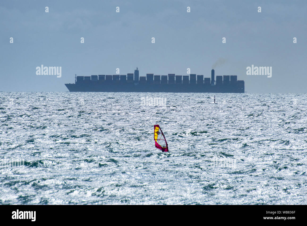 Einen dramatischen Kontrast eines einsamen Windsurfer vor einem riesigen Containerschiff an der West Wittering, West Sussex, England, Vereinigtes Königreich Stockfoto