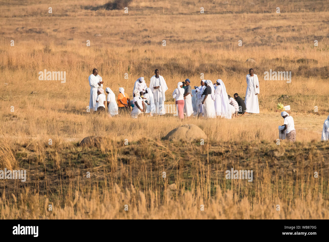 Afrikanischen schwarzen Menschen in weißen Kleidern oder Kleidungsstücke, die eine religiöse Zeremonie im Freien oder bei Sonnenuntergang im Winter Johannesburg, Gauteng gekleidet Stockfoto