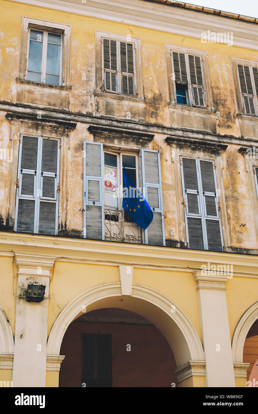 Ein von der EU mit der Blauen Flagge von einem Verblasster Glanz hellgelbe Fassade Gebäude mit Fenstern in Italien hängen. Stockfoto