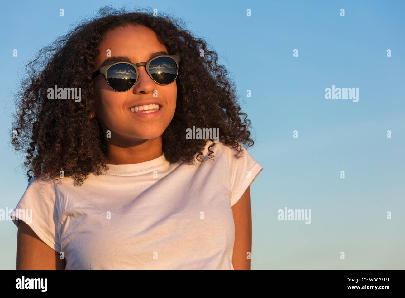 Mischlinge biracial African American Girl Teenager weibliche junge Frau mit perfekte Zähne bei Sonnenuntergang oder Sunrise Sonnenbrille tragen Stockfoto