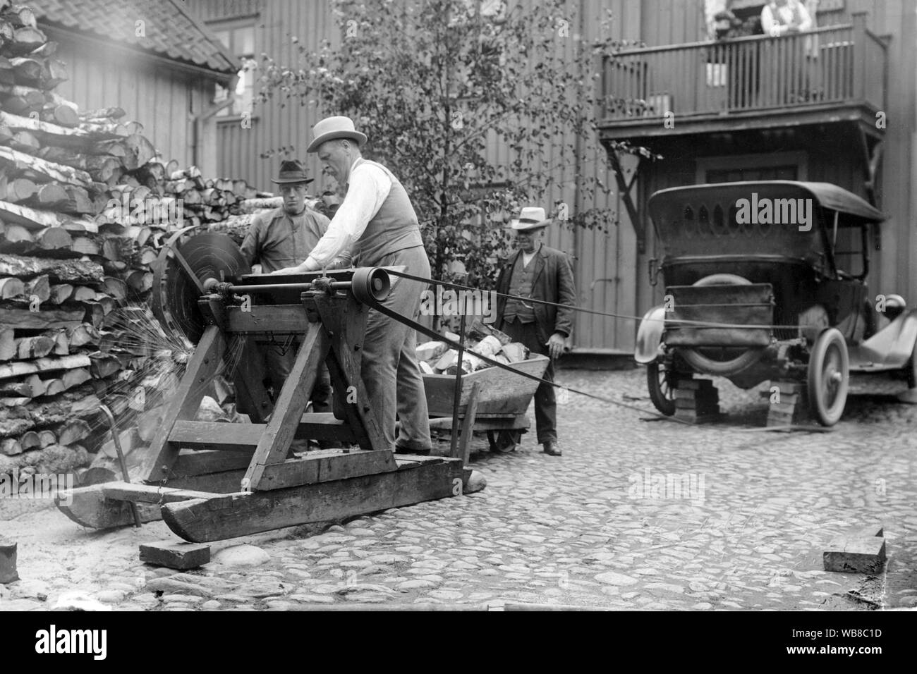 Innovativ in den 1920er Jahren. Eine Gruppe von Männern sind Brennholz in der Straße. Sie verwenden das Hinterrad des Autos als Kraft an die Säge und einen Riemen die beiden anschließen. Eine innovative Lösung. Stockfoto