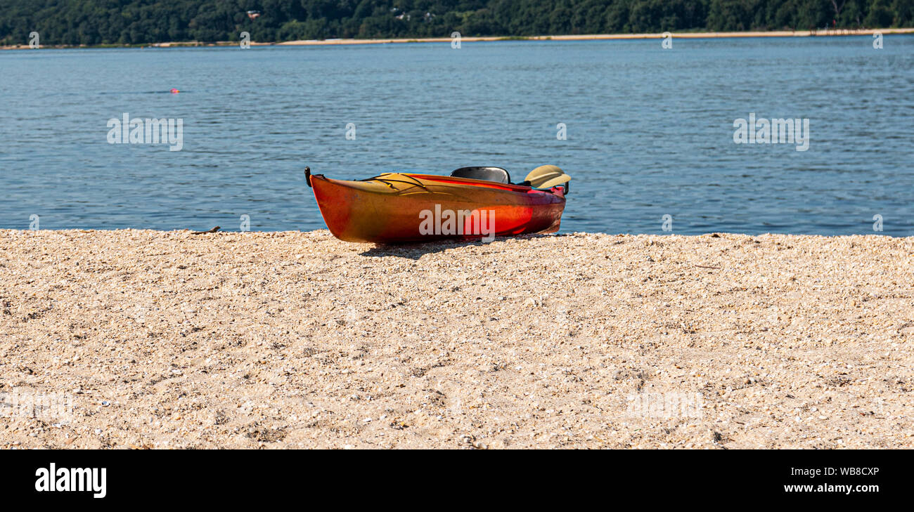 Eine einzelne orange Kajak auf der Sand am Strand mit blauem Wasser im Hintergrund. Stockfoto