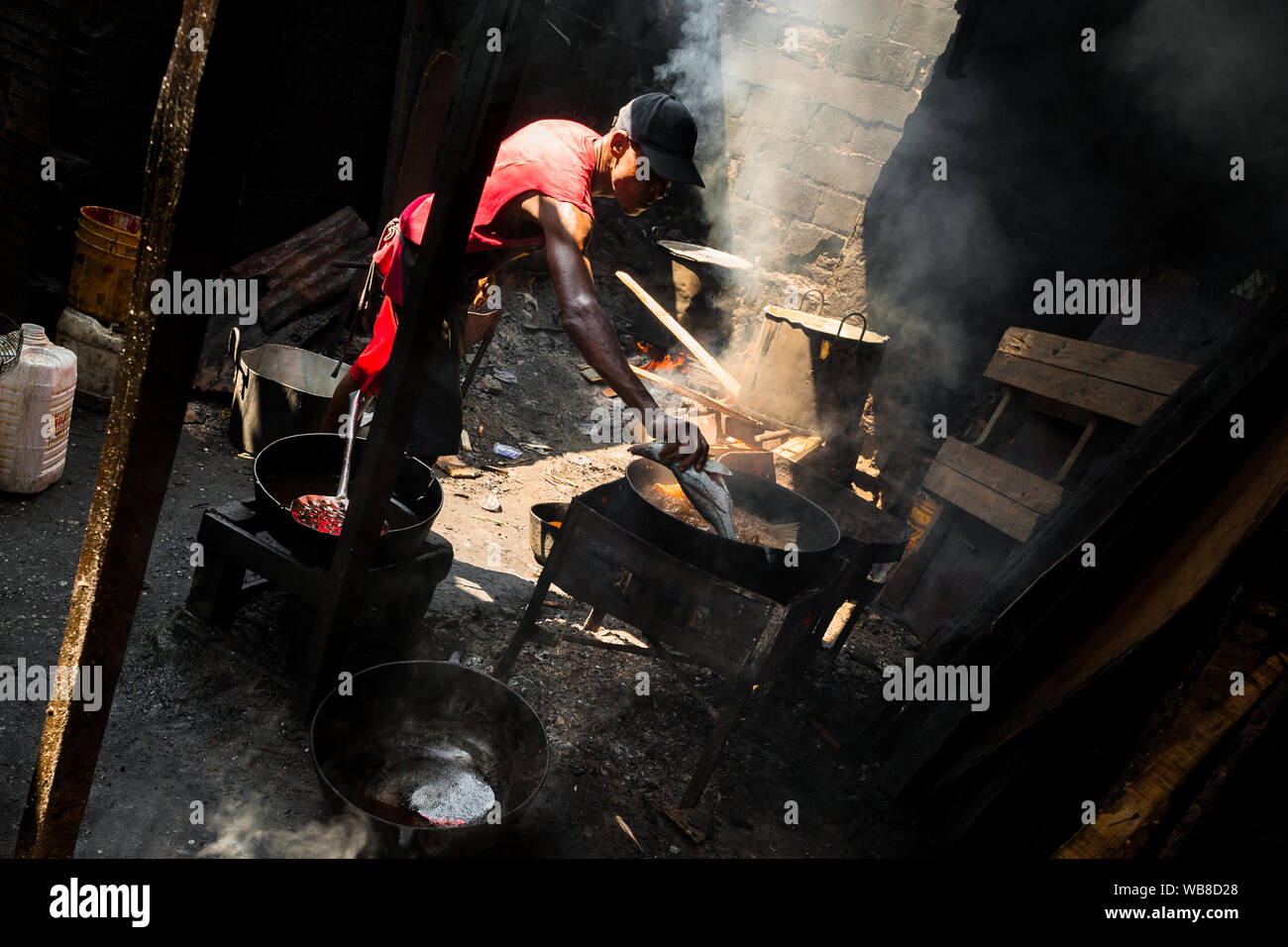 Eine afrokolumbianischen Koch wirft einen Fisch in kochendes Öl in einem Street Restaurant im Markt der Bazurto in Cartagena, Kolumbien. Stockfoto