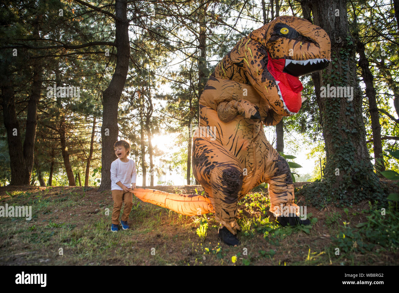Vater und Sohn spielen im Park, mit einem Dinosaurier Kostüm, Spaß mit der Familie im Freien Stockfoto