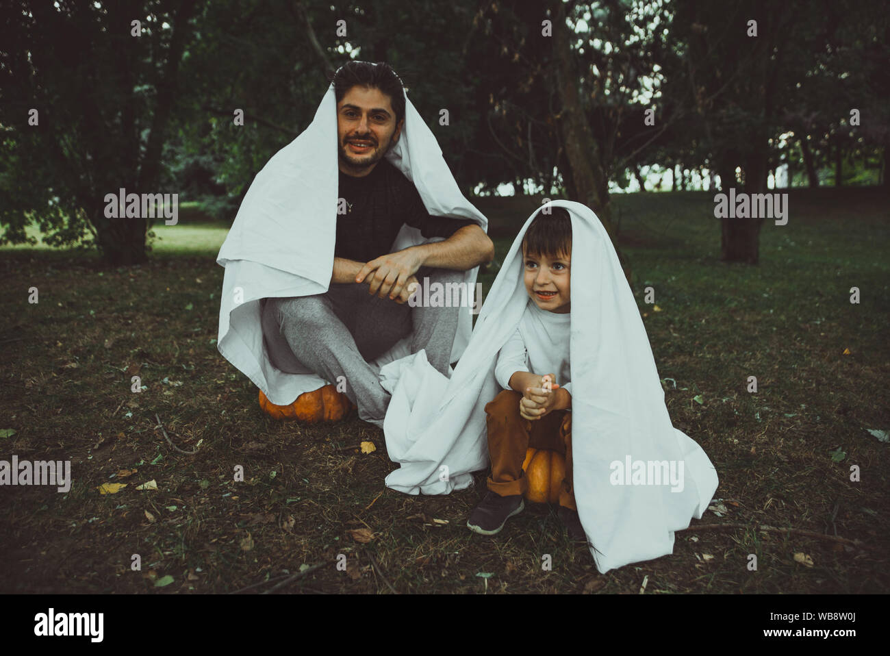 Vater und Sohn spielen Geister mit weißen Laken im Garten, konzeptionelle Fotos über Halloween Feiertage Stockfoto