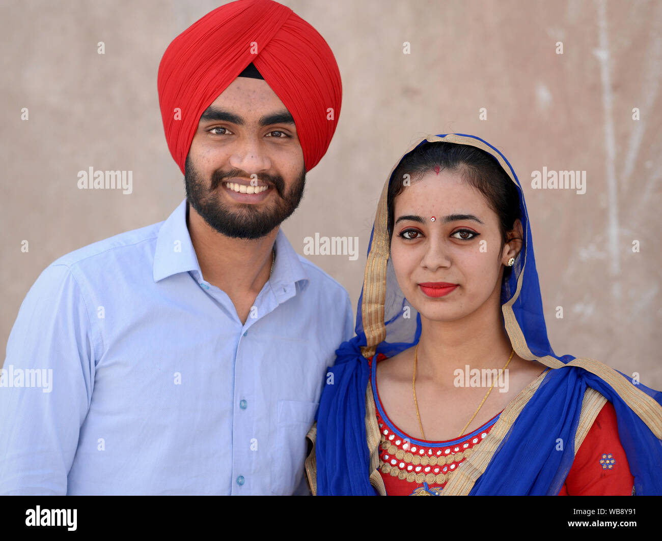 Modebewusste junge indische Sikh Paar trägt passenden Outfits in den Farben Rot und Blau und Lächeln für die Kamera. Stockfoto