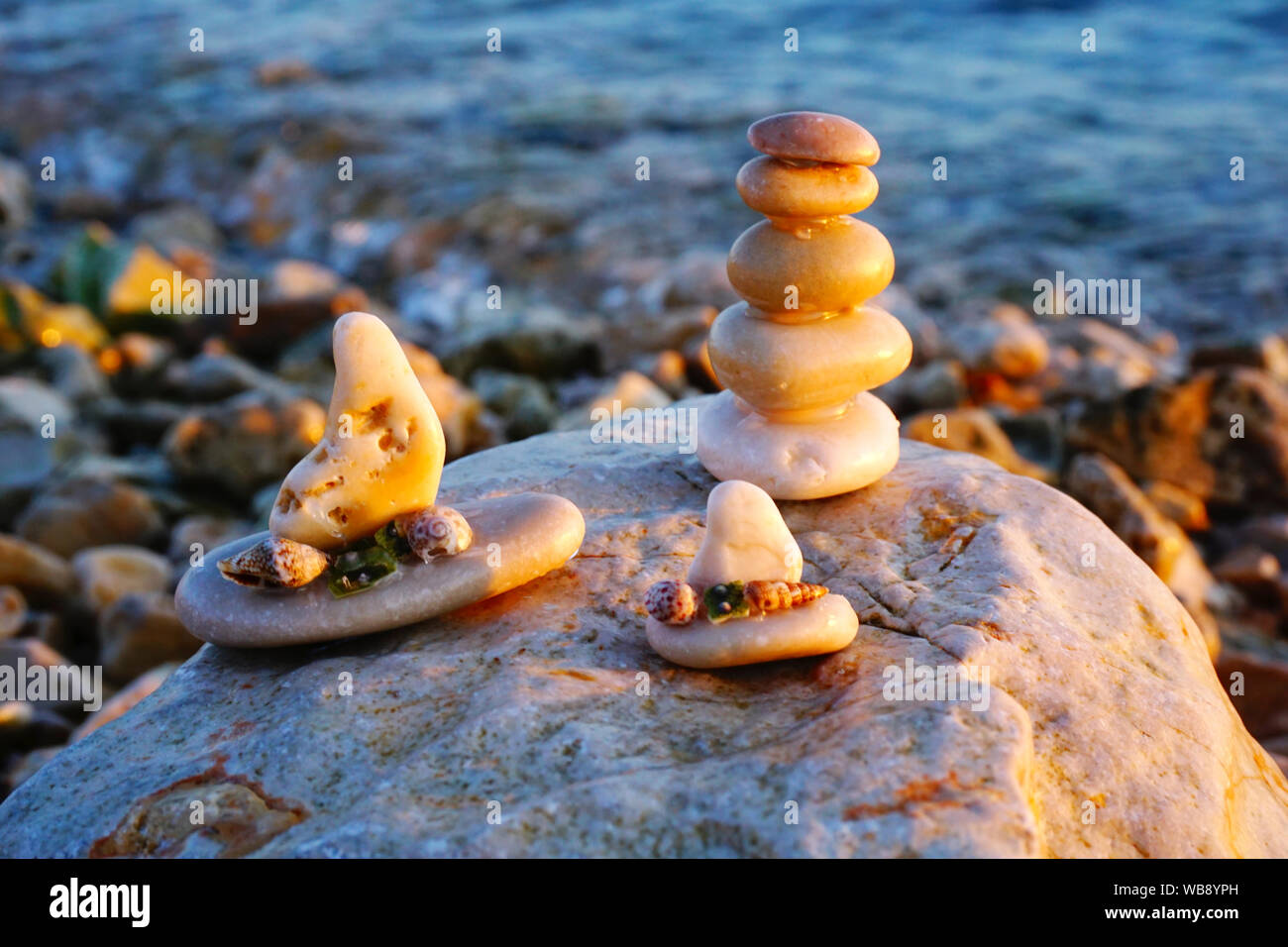 Handwerk Souvenirs aus Kieselsteinen. Sonnenuntergang Reflexion über das Meer Strand mit Kiesel Kunst, kleine Steine stapeln und dekorative Boote aus kleinen Steinen ein Stockfoto