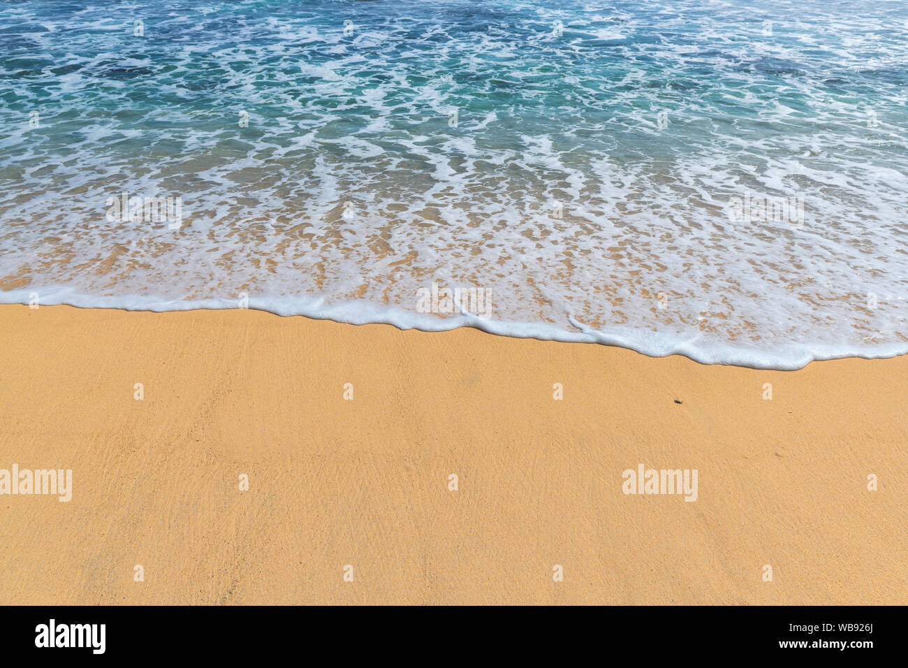 Weiche Wellen mit Schaumstoff am Sandstrand. Stockfoto