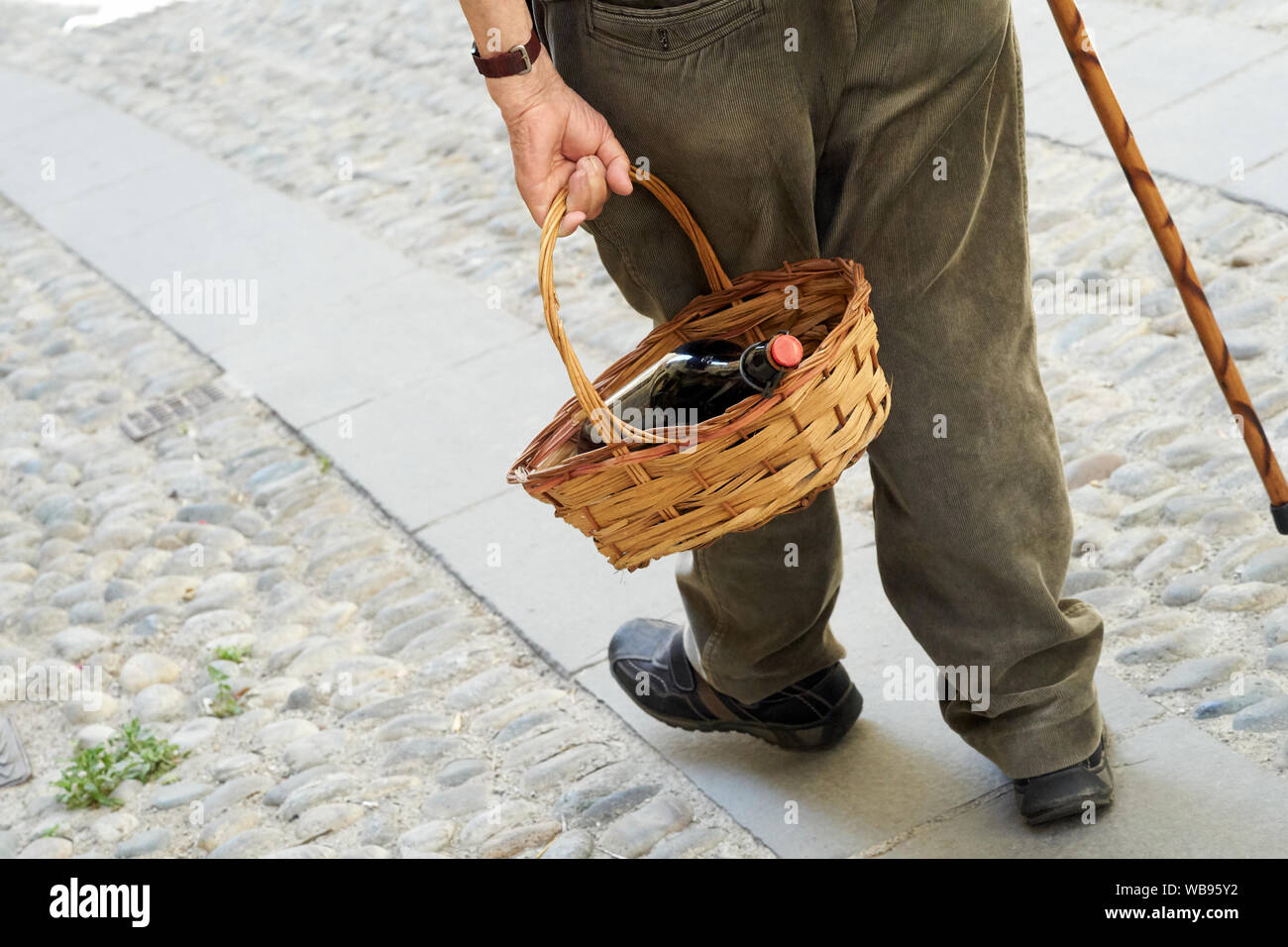 Ein älterer Mann mit einem Korb in der Hand mit einer Flasche Wein Stockfoto