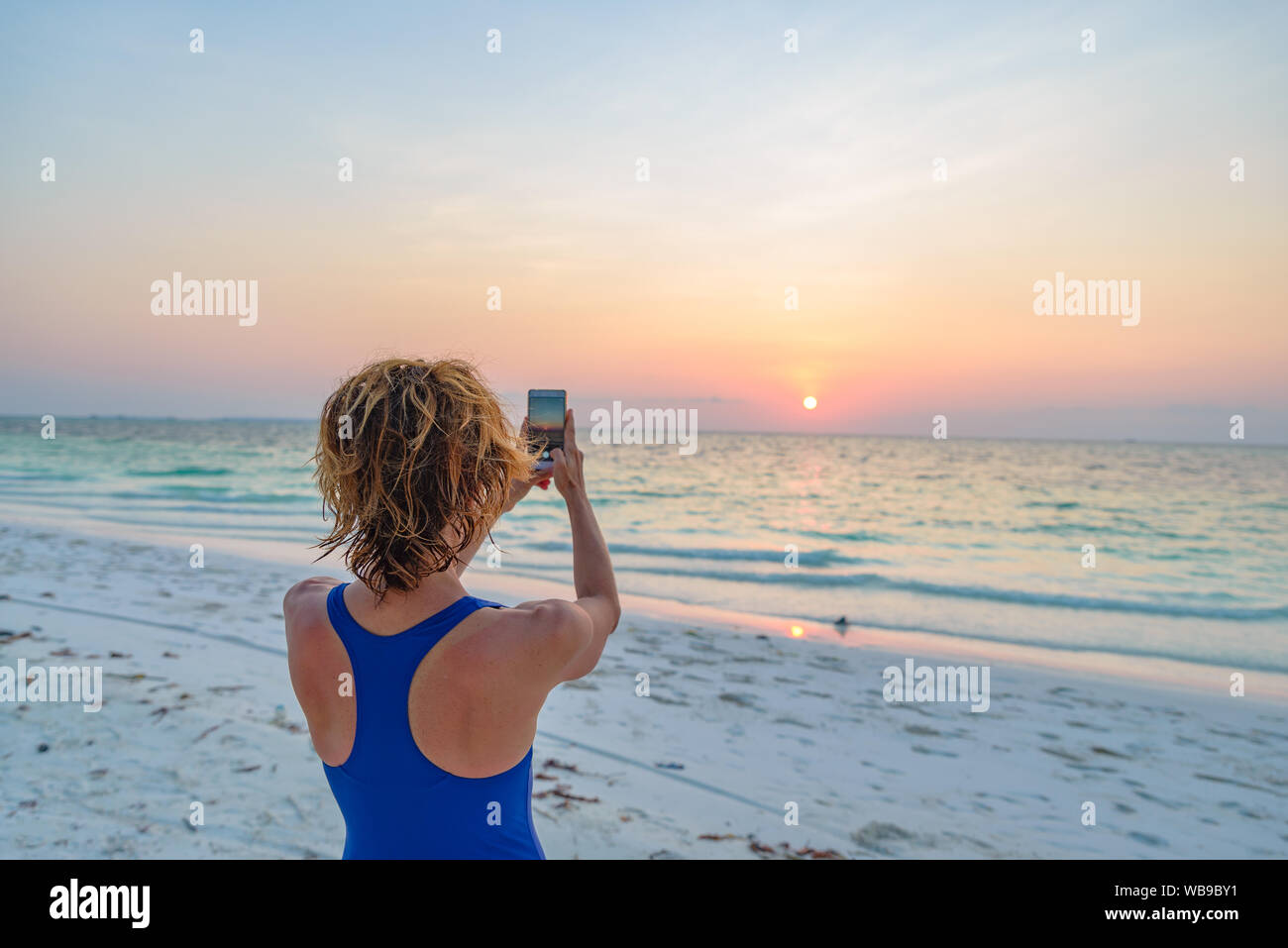 Frau unter Foto mit Smartphone der romantischen Himmel bei Sonnenuntergang auf Sand Strand, Rückansicht, echte Menschen rund um die Welt reisen. Indonesien tropischen dest Stockfoto