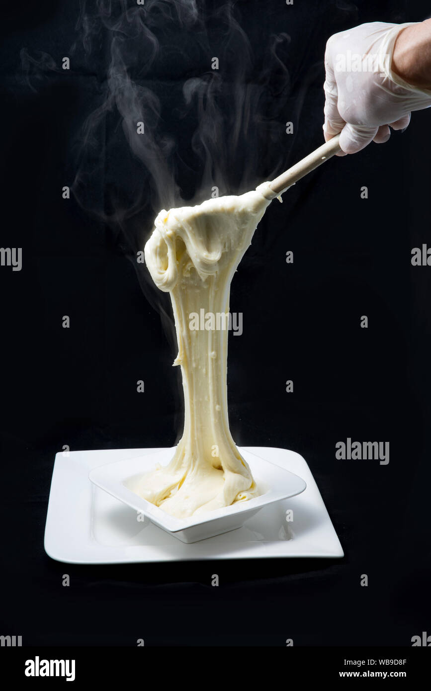 Ein hoher Kontrast künstlerische Held Schuß von frischem, heißem Käse serviert auf einem Tablett mit Rauch aus der gestreckten Käse auf einen minimalen Weiß zurück Stockfoto