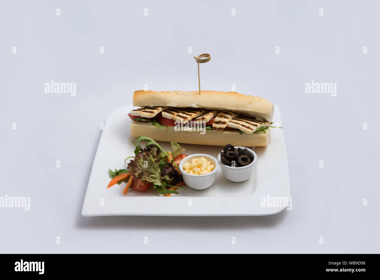 Einen niedrigen Kontrast hero Schuß eines gegrilltem Halloumi Käse Baguette mit Oliven & Salat auf der Seite, auf einer minimalen weißen Hintergrund mit einem Winkel von 45 Grad f Stockfoto