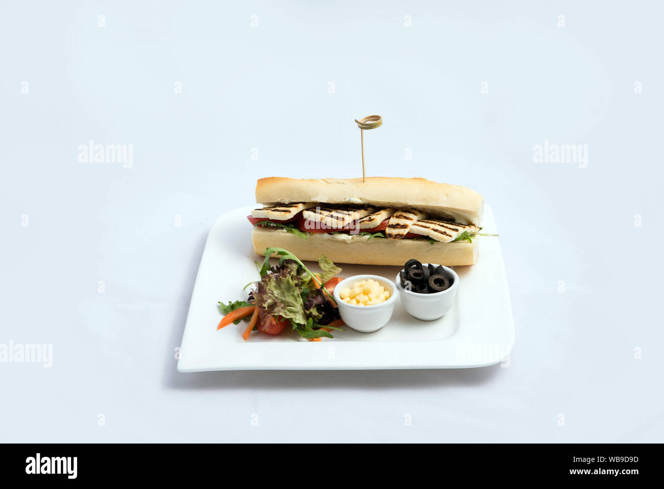 Ein hoher Kontrast hero Schuß eines gegrilltem Halloumi Käse Baguette mit Oliven & Salat auf der Seite, auf einer minimalen weißen Hintergrund mit einem Winkel von 45° Stockfoto