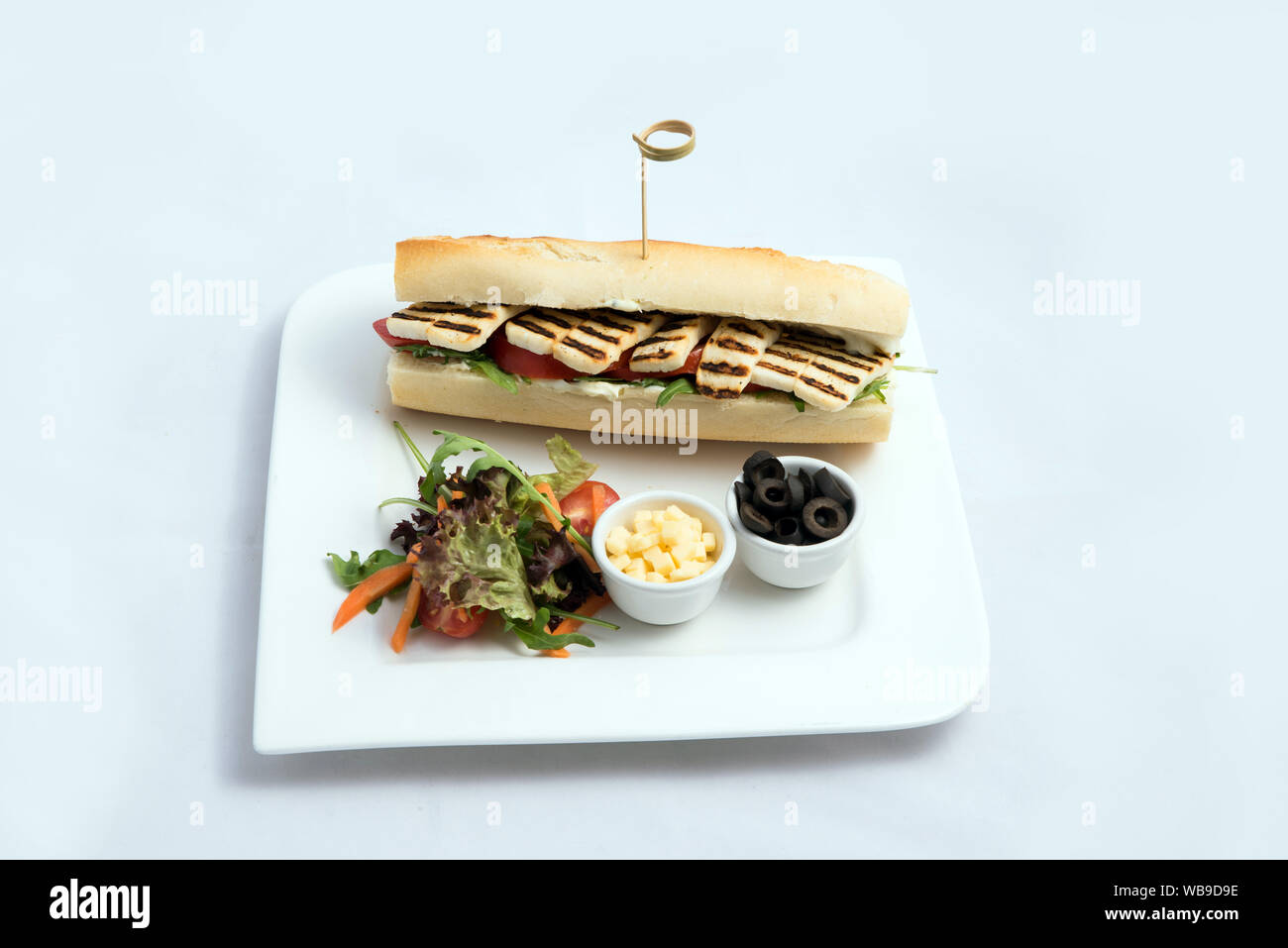 Ein hoher Kontrast hero Schuß eines gegrilltem Halloumi Käse Baguette mit Oliven & Salat auf der Seite, auf einer minimalen weißen Hintergrund mit einem 60 Grad Winkel Stockfoto