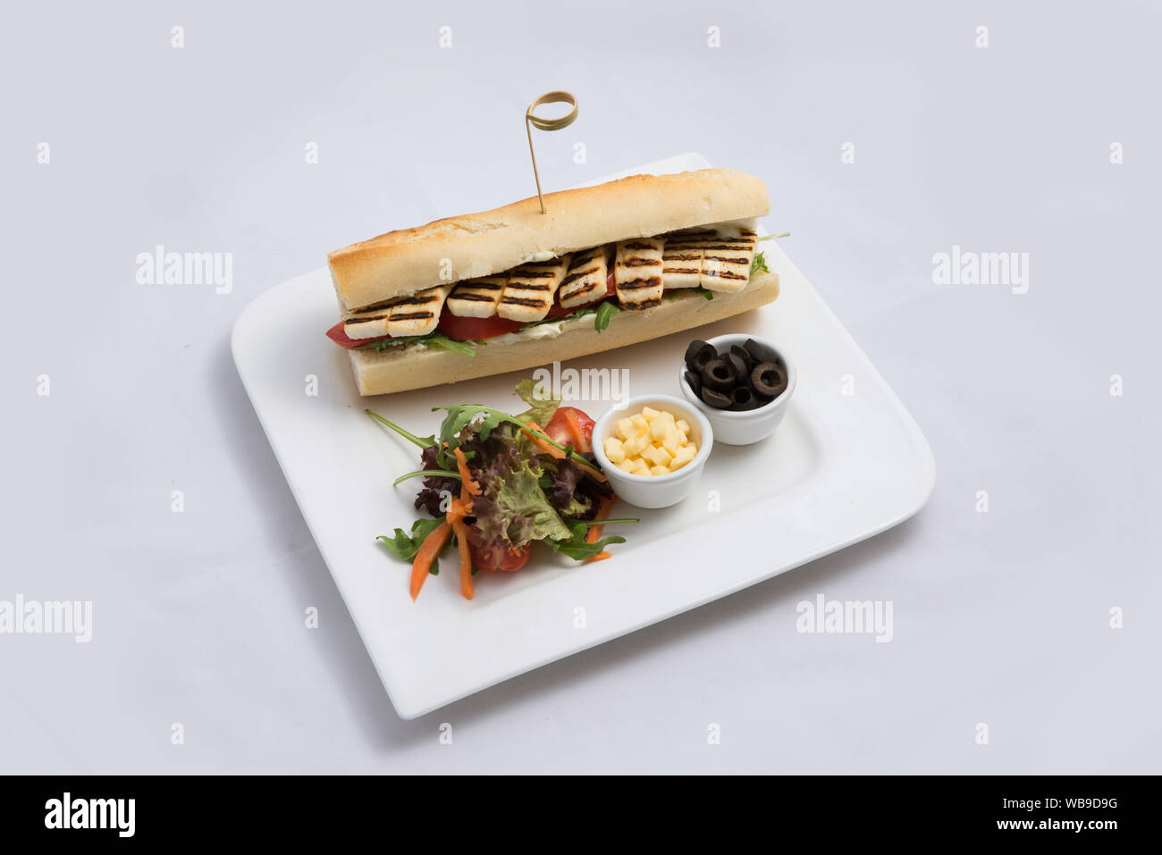 Einen niedrigen Kontrast hero Schuß eines gegrilltem Halloumi Käse Baguette mit Oliven & Salat auf der Seite, auf einer minimalen weißen Hintergrund mit 60 Grad f Stockfoto