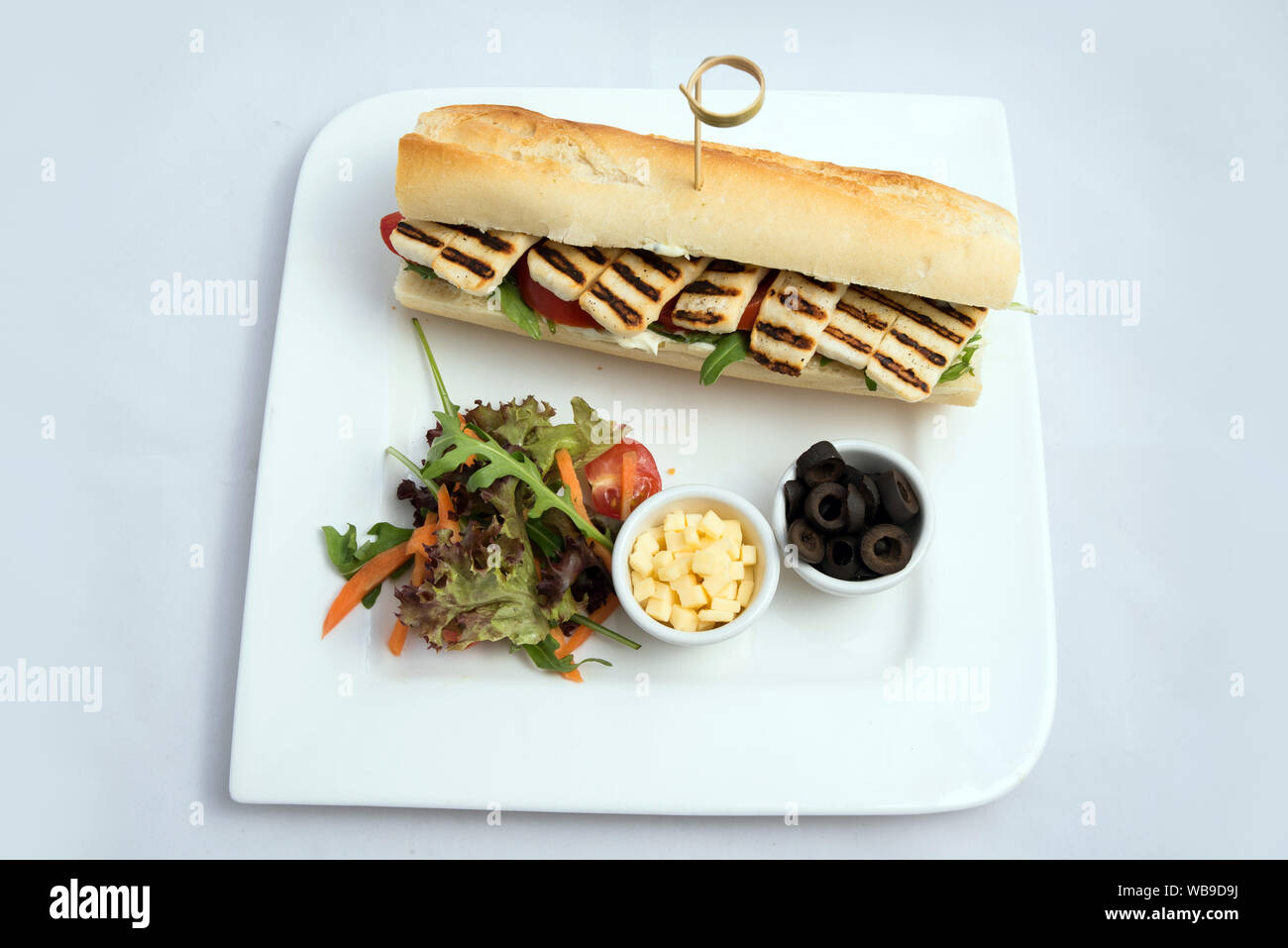 Ein hoher kontrast vertikale hero Schuß eines gegrilltem Halloumi Käse Baguette mit Oliven & Salat auf der Seite, auf einer minimalen weißen Hintergrund mit einem 90 Dagr Stockfoto